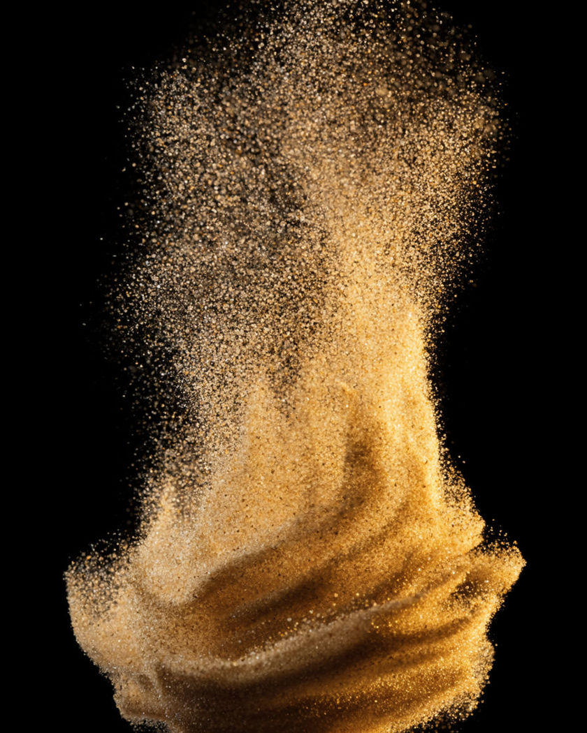 A rising column of golden sand grains churning upward and catching a hard side light on a black ground