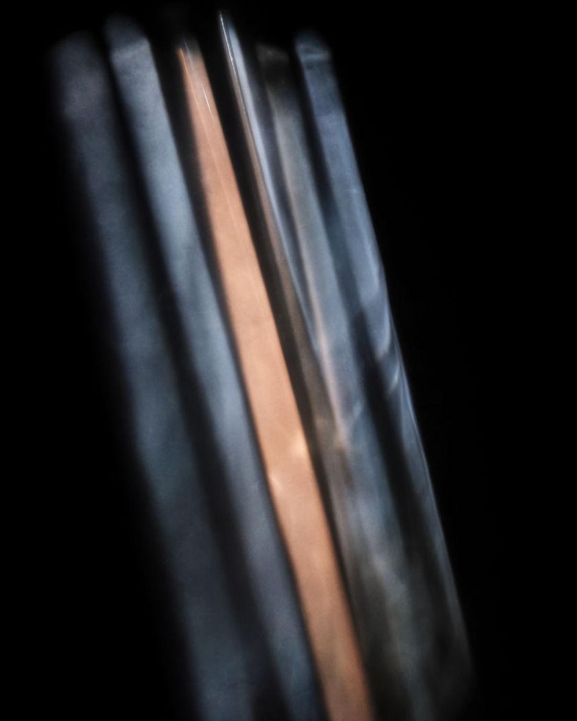 Long soft-edged bars of shadow raking diagonally across a pure black ground with one warm slash of light between them