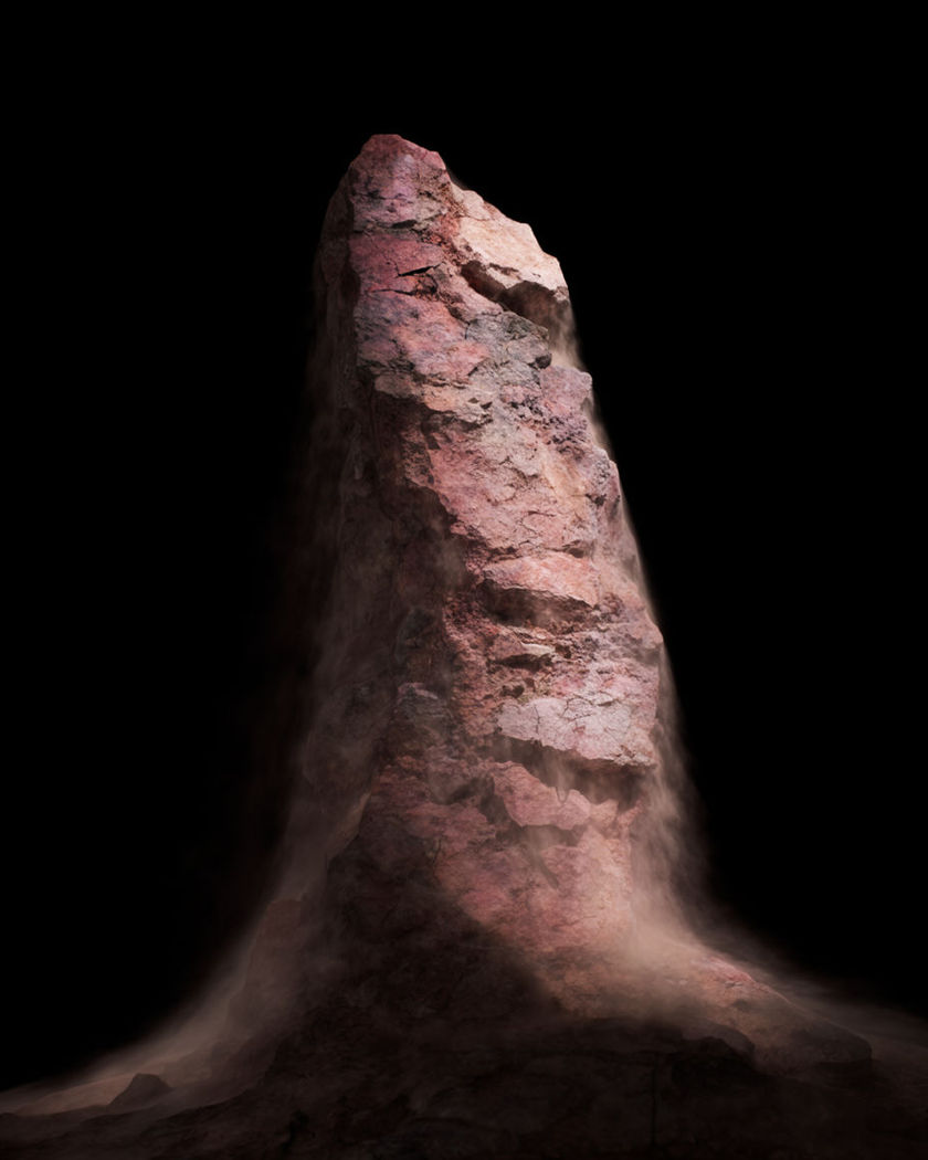A jagged column of rough stone thrusting upward with dust cascading off its cracked sides against a black ground