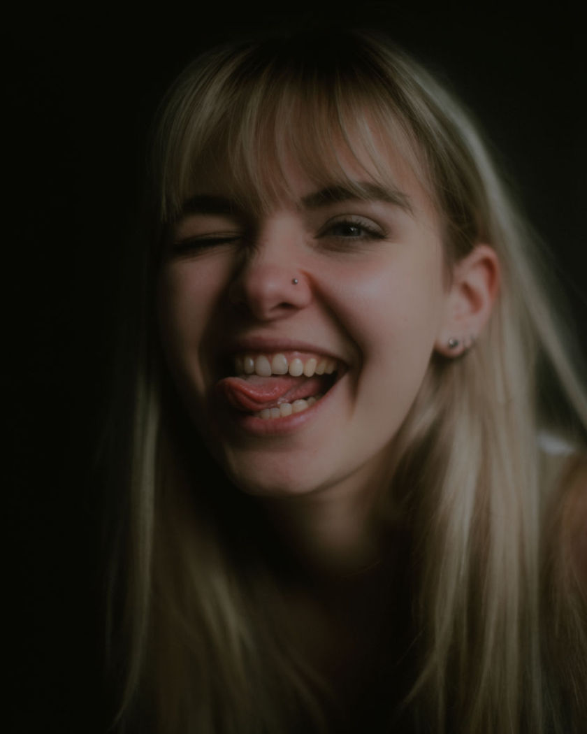 A playful close portrait mid-laugh with a tongue-out grin and a wink, caught on a fast camera snap
