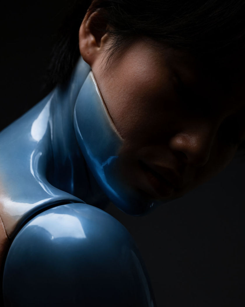 A person mid-transformation, half real skin and half glossy plastic, jointed seams appearing at the shoulder