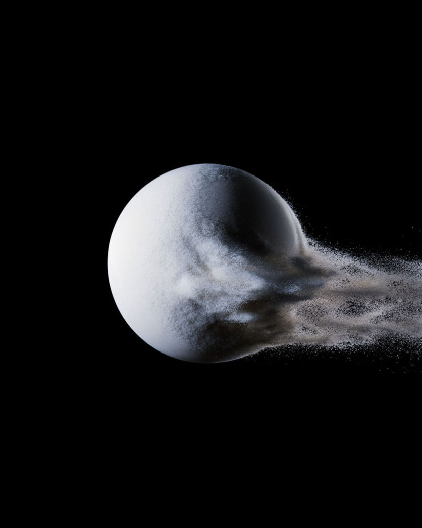 A solid luminous sphere with its windward side breaking into fine dust that streams away on a black ground