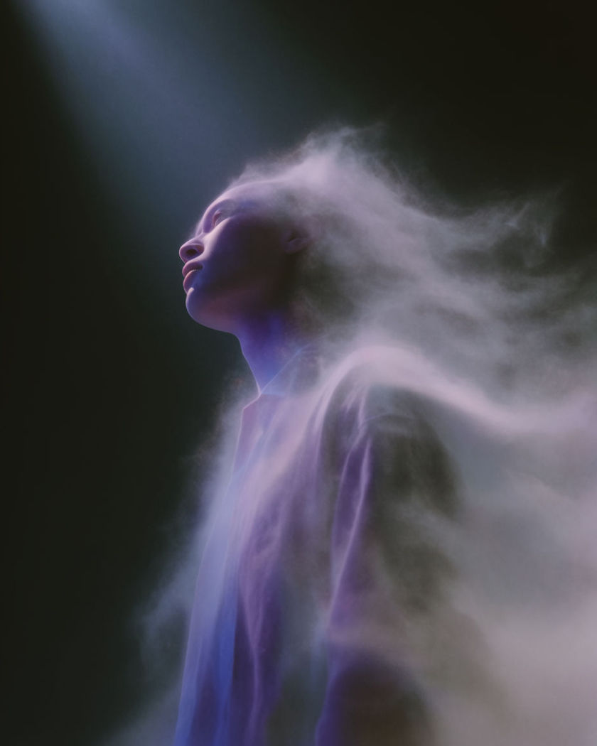 A figure dissolving from the edges into soft drifting mist that catches a shaft of light