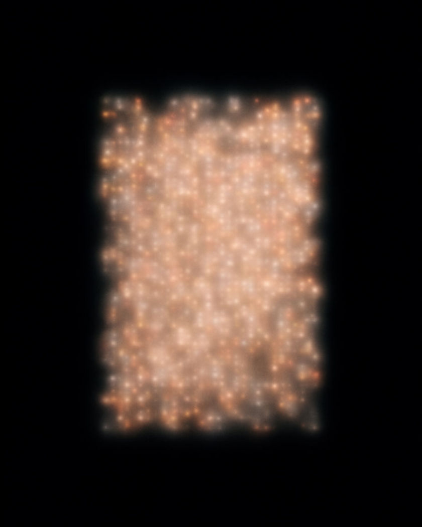 A field of small warm lights shimmering in and out of focus against a pure black ground