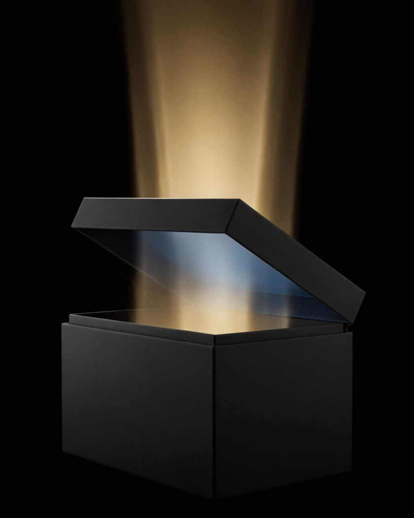 A plain matte black box with its lid lifted and hovering a hand width above it on a black ground